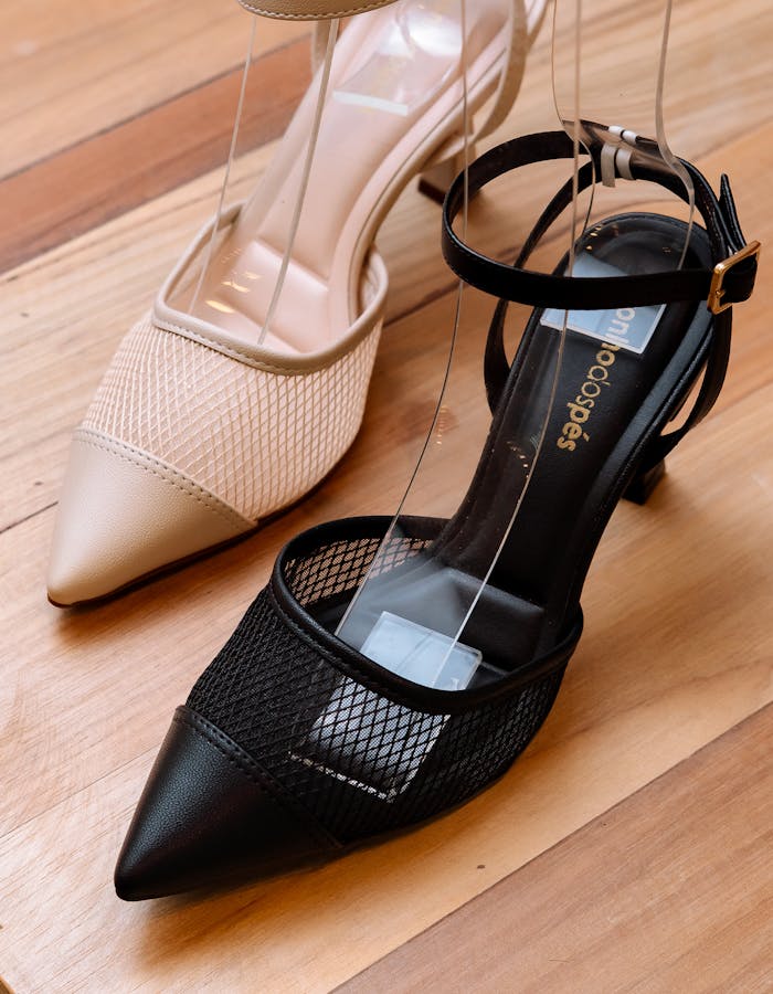 Elegant black and beige mesh heeled shoes displayed on a wooden floor for fashion showcase.